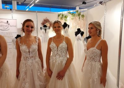 Drei Frauen präsentieren Spitzen-Brautkleider auf Messe