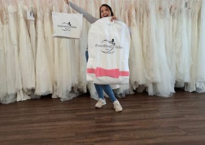 Frau zeigt Kleidersack vor Brautkleidern